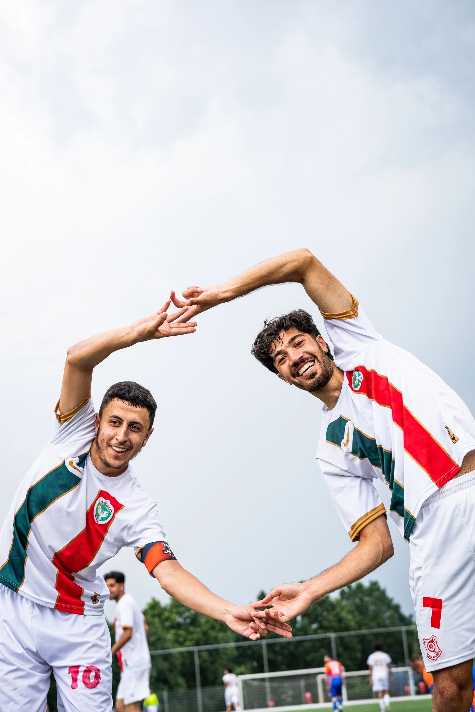 Twee spelers in wit-groen-rode shirts maken samen een hart met hun armen