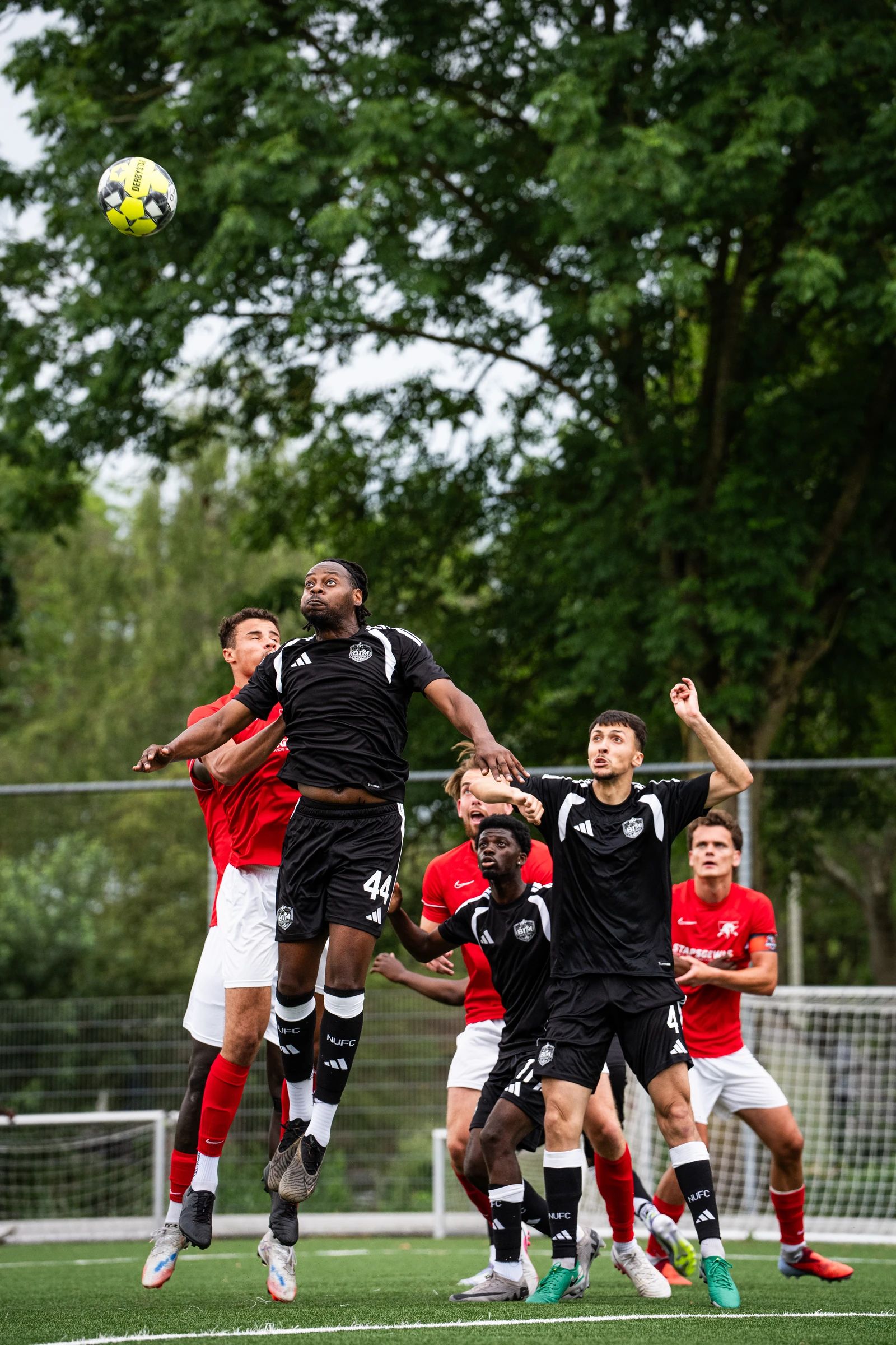 Spelers in rood en zwart springen samen naar een hoge bal