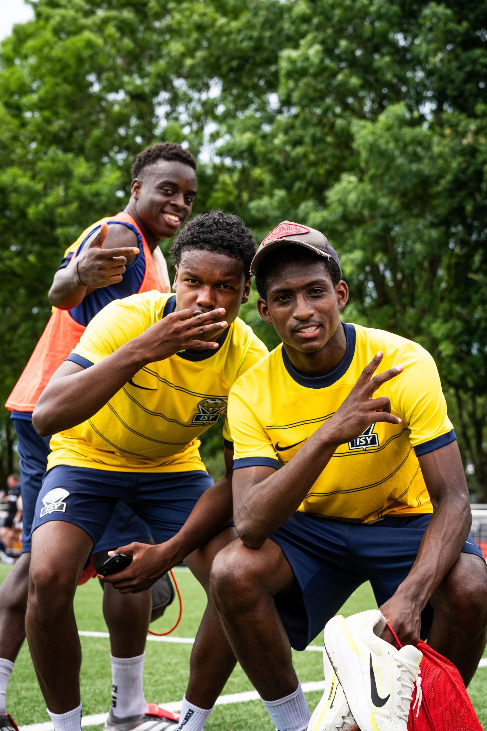 Drie spelers maken lachend een gebaar naar de camera op de AFA Cup van 2026, twee van hen in gele shirts