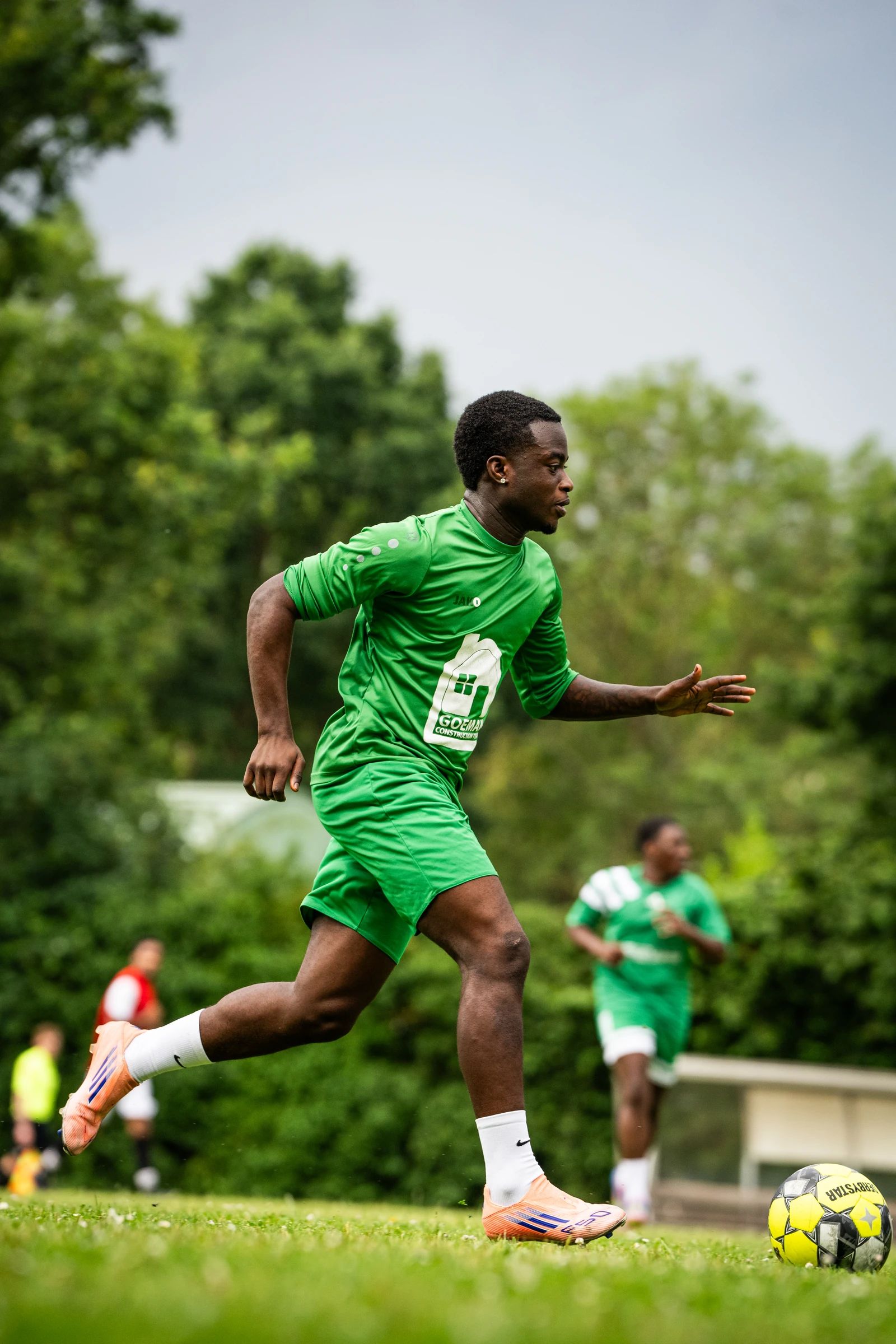 Een speler in een groen shirt sprint naar de bal