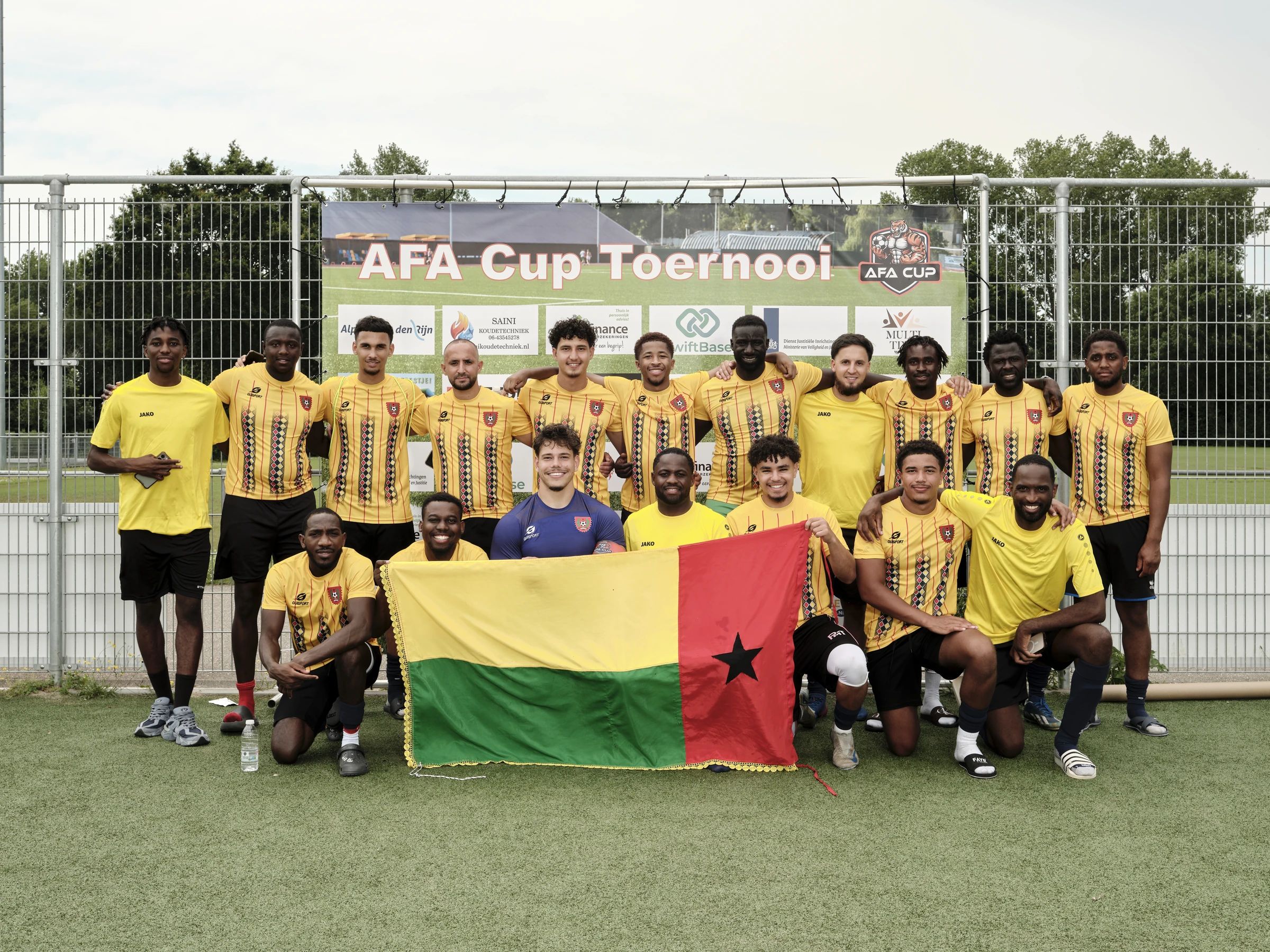Een team in geel-rode shirts met de vlag van Guinee-Bissau op de teamfoto van 2026