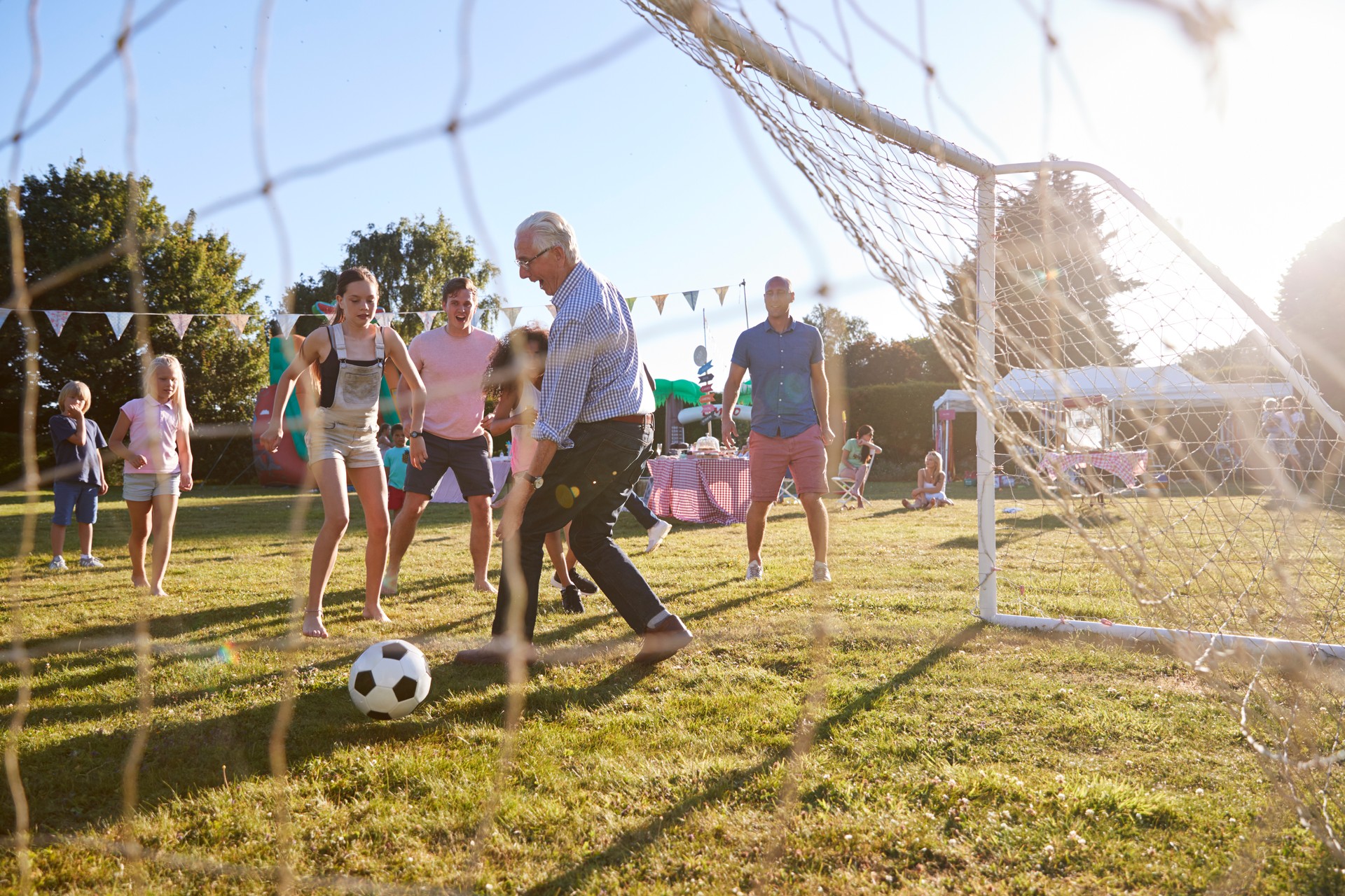 Children Playing Football Match With Father And Grandfather At Summer Garden Fete