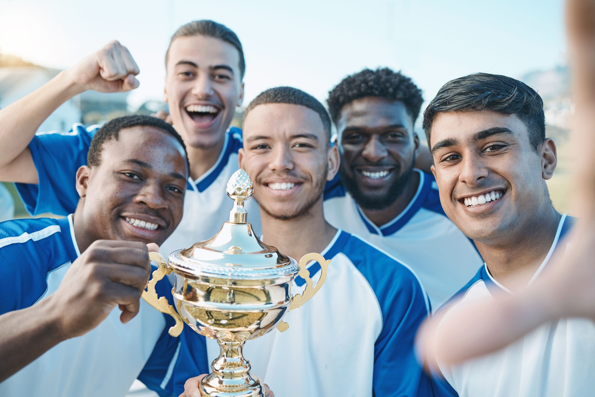 Sports group, soccer trophy and selfie of team on field for game award or prize outdoor. Football player, club and diversity champion men portrait for sport competition win, success and achievement Sports group, soccer trophy and selfie of team on field for game award or prize outdoor. Football player, club and diversity champion men portrait for sport competition win, success and achievement